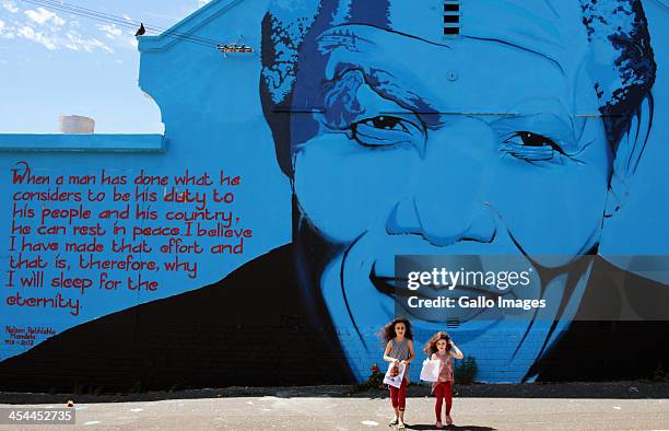 Two girls seen at a mural of Nelson Mandela by graffiti artist Mak1One on December 7, 2013 in Cape Town, South Africa. The Father of the Nation,...