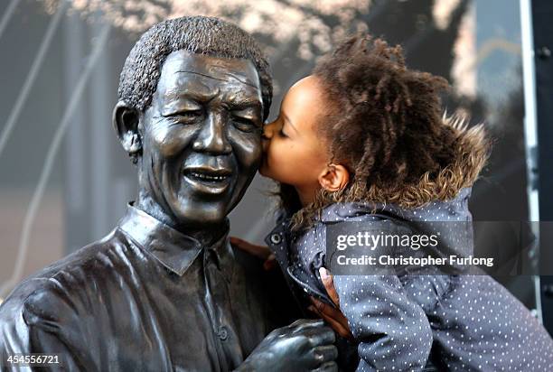 Young South African girl names Malika is lifted by her mother to kiss a statue of former South African President Nelson Mandela before a service...