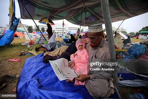 Pakistani anti-government protestor reads a newspaper in a tent during his waiting at the parliament garden within the ongoing protests in Islamabad,...