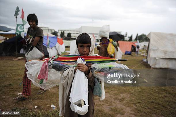 Pakistani kid carrying umbrellas is seen during leave-taking of ome Pakistani anti-government protestors from the parliament garden upon calling of...