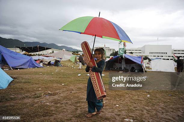 Pakistani kid with an umbrella and rush mat is seen during leave-taking of ome Pakistani anti-government protestors from the parliament garden upon...