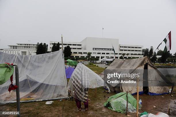 Pakistani anti-government protestor tries to shelter from rain with a plastic canvas during the waiting at the parliament garden within the ongoing...