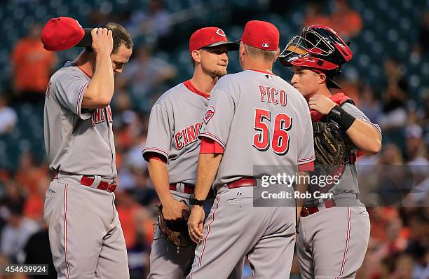 Jack Hannahan , catcher Tucker Barnhart and pitching coach Jeff Pico talk with starting pitcher Mike Leake of the Cincinnati Reds during the first...