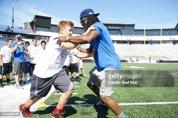 Portrait of Seattle Seahawks cornerback Richard Sherman demonstrating drill with children during Wilson's Passing Academy youth camp at Husky...