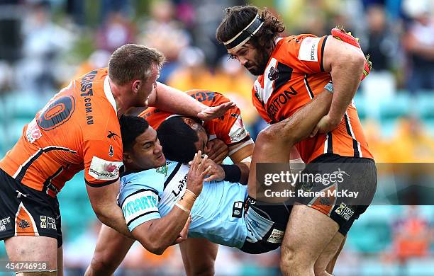 Ricky Leutele of the Sharks is tackled by Matt Lodge and Aaron Woods of the Tigers during the round 26 NRL match between the Wests Tigers and the...
