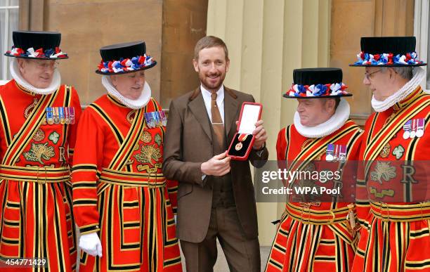 Sir Bradley Wiggins CBE holds his Knighthood award as he is surrounded by Yeomen of the Guard after it was presented to him by Queen Elizabeth II at...