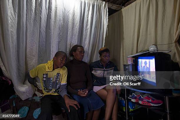 Family watch the official memorial service for Nelson Mandela on a television inside their makeshift home in Alexandra Township on December 10, 2013...