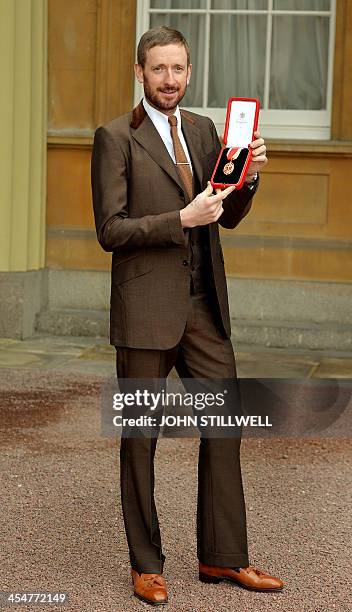 British cyclist Bradley Wiggins poses holding his medal after being appointed a Knights Bachelor by Britain's Queen Elizabeth II at an investiture...
