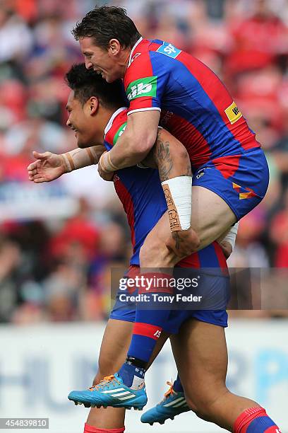 Kurt Gidley of the Knights jumps onto the back of team mate Joey leilua after scoring a try during the round 26 NRL match between the Newcastle...