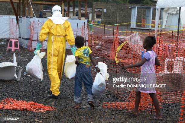 Medical worker wearing a protective suit carries bags followed by Ebola infected children in the high-risk area of the Elwa hospital runned by...