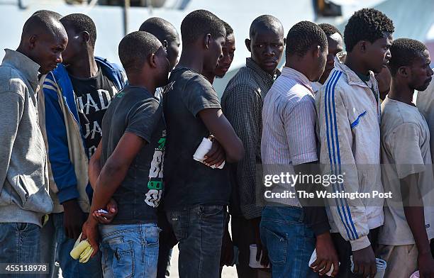 African migrant men wait in line to have medical evaluations after disembarking from the Italian Navy ship Foscari on August 23, 2014 in Portopalo di...
