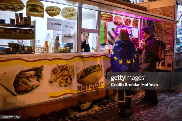 Woman wrapped in a European Union flag stops at a hot dog stand near Independence Square on December 11, 2013 in Kiev, Ukraine. Thousands of...