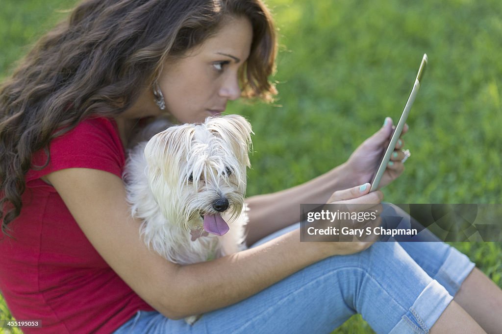 Hispanic woman using tablet with dog on lap