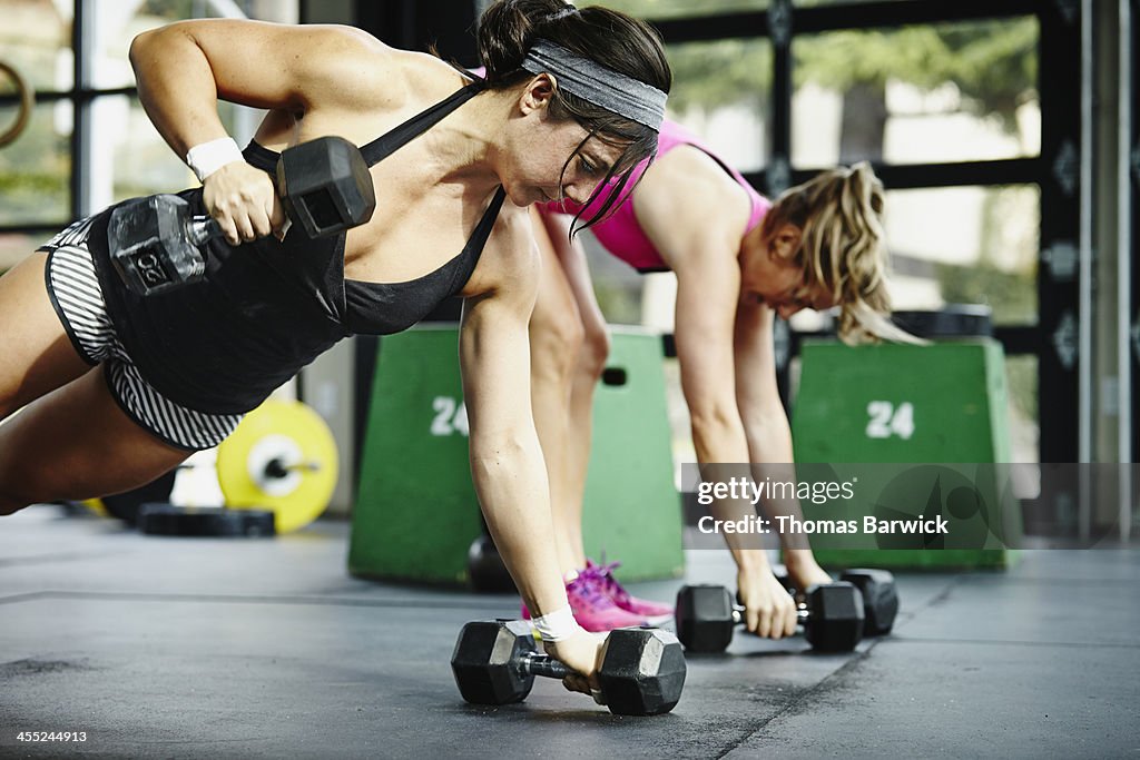 Two women doing pushups with dumbbells in gym