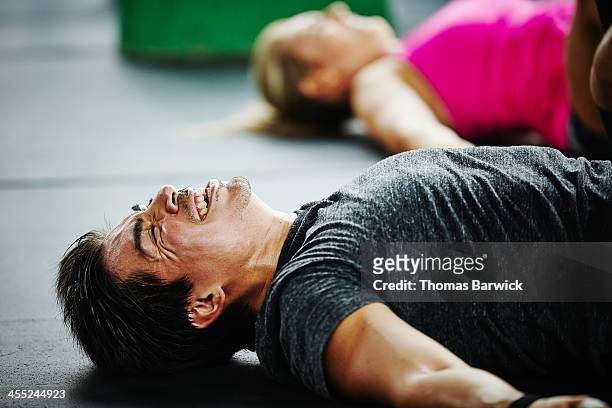 man laughing and grimacing lying on floor of gym - sports pain stock-fotos und bilder