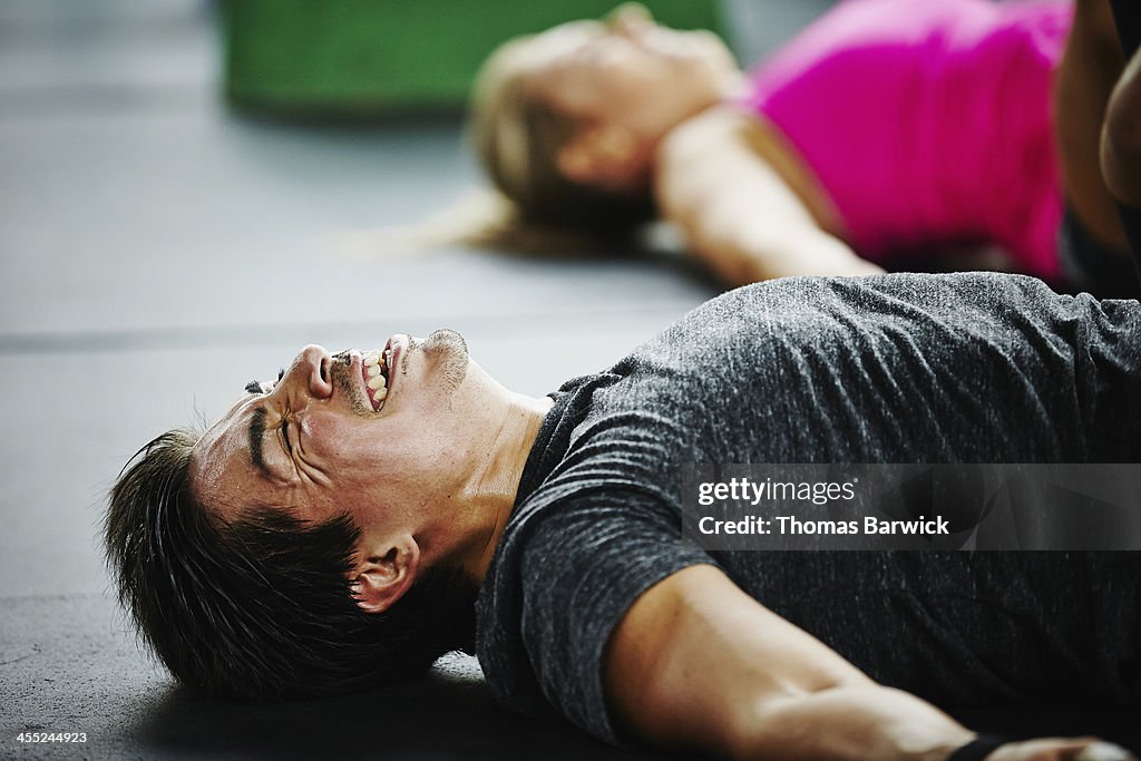 Man laughing and grimacing lying on floor of gym