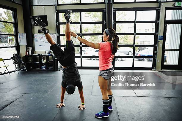 Woman spotting man doing handstand in gym