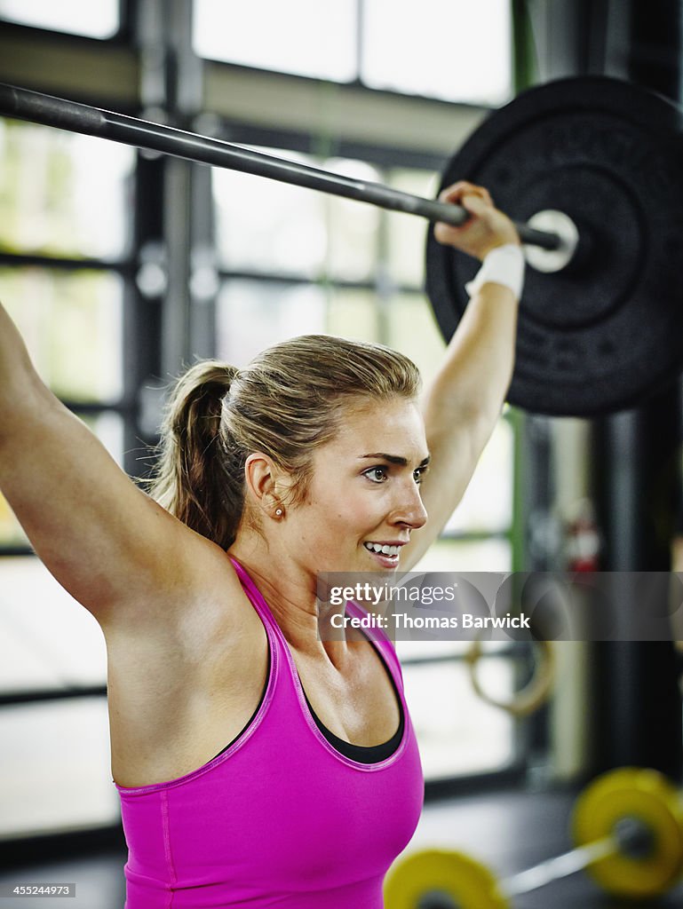 Woman pressing barbell over head in Gym gym