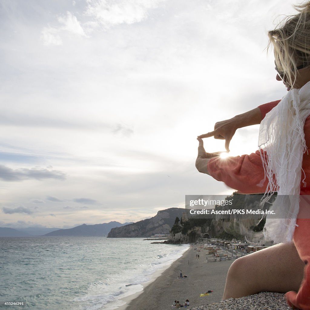 Woman franes beach view and sunrise using hands