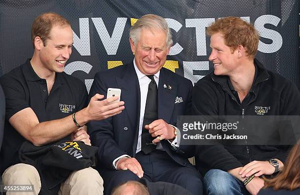 Prince William, Duke of Cambridge, Prince Harry and Prince Charles, Prince of Wales look at a mobile phone as they watch the athletics at Lee Valley...