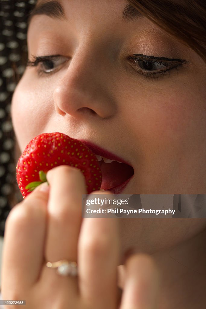 A young woman eating a strawberry