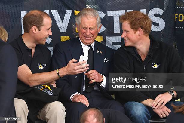 Prince William, Duke of Cambridge, Prince Charles, Prince of Wales & Prince Harry look at a mobile phone as they watch the athletics during the...