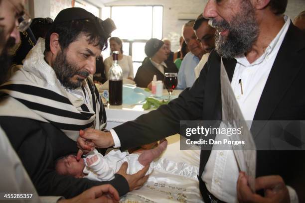 During a brit milah ceremony, a mohel smiles and uses his finger to pacify an eight-day-old Jewish boy following circumcision, Jerusalem, Israel,...