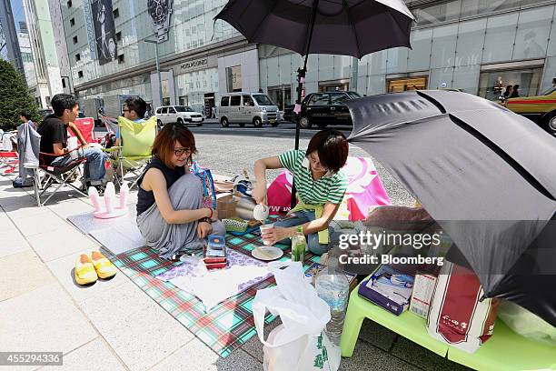 Asumi Katakura, left, looks on as Yayoi Hayase pours a drink while they wait in line outside Apple Inc.'s Ginza store ahead of the launch of the...