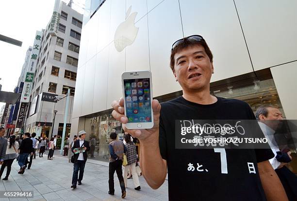 Apple fan Tetsuya Tamura holds a China made "iPhone 6" as he wears a t-shirt with writing translating to "7 days remaining for iPhone 6 launch" as he...