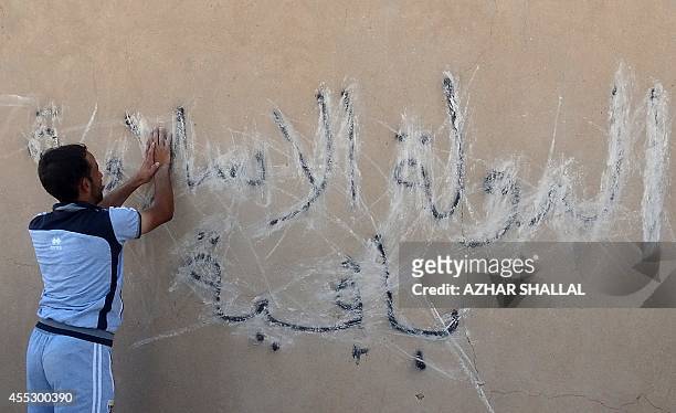 An Iraqi man scribbles on September 10, 2014 over graffiti on the wall reading in Arabic, "the Islamic State is staying after Iraqi government forces...