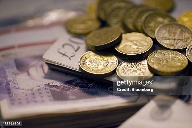 Sterling one pound coins and bundles of 20 pound sterling banknotes are arranged for a photograph inside a Travelex store, operated by Travelex...