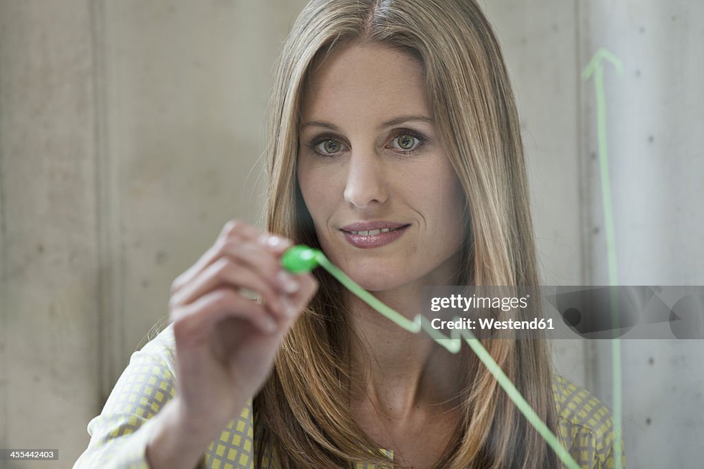 Germany, North Rhine Westphalia, Cologne, Businesswoman drawing graph on glass, smiling