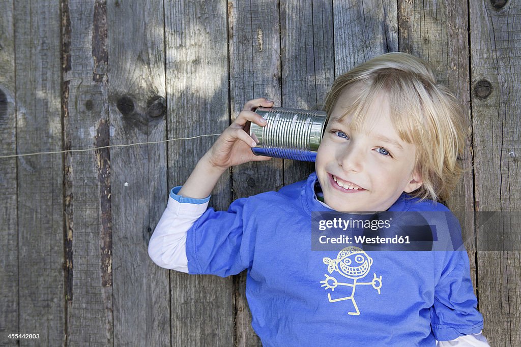 Germany, North Rhine Westphalia, Cologne, Portrait of boy listening to tin can phone, smiling
