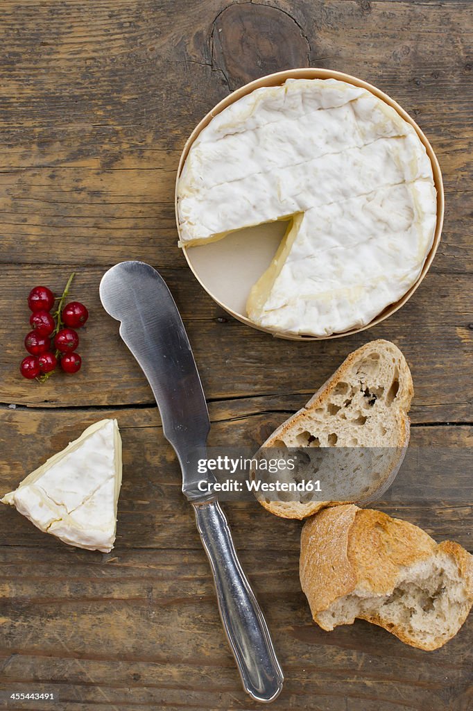 Camember cheese with red currant and baguette on wooden table