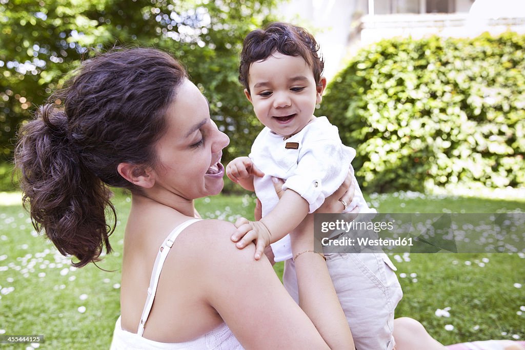 Mother cuddling her baby boy on grass, smiling