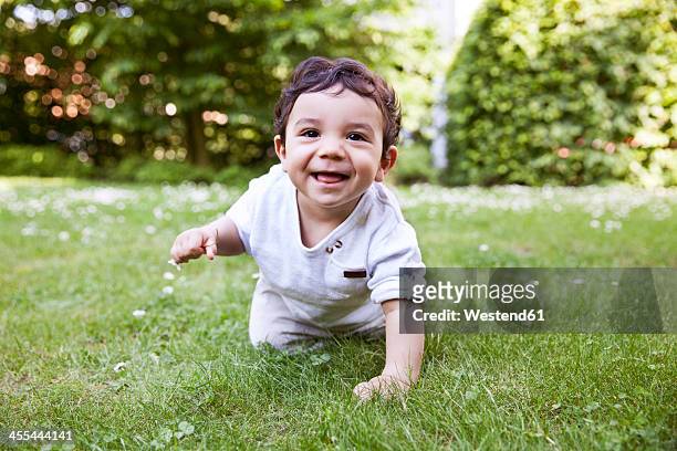 baby boy crawling on grass, smiling - crawling stock-fotos und bilder