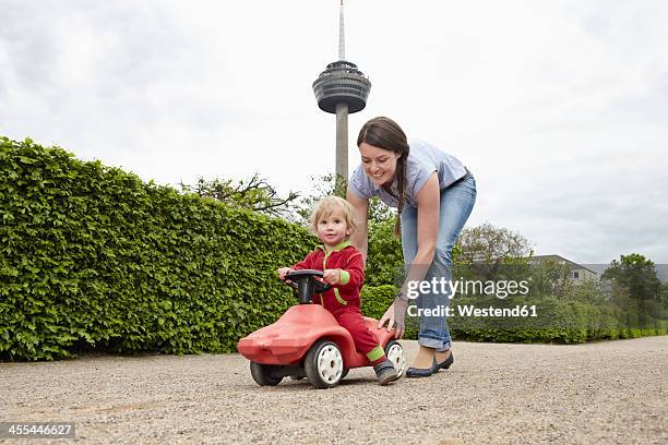 germany, cologne, mother carrying daughter in toy car, smiling - macchina a pedali foto e immagini stock