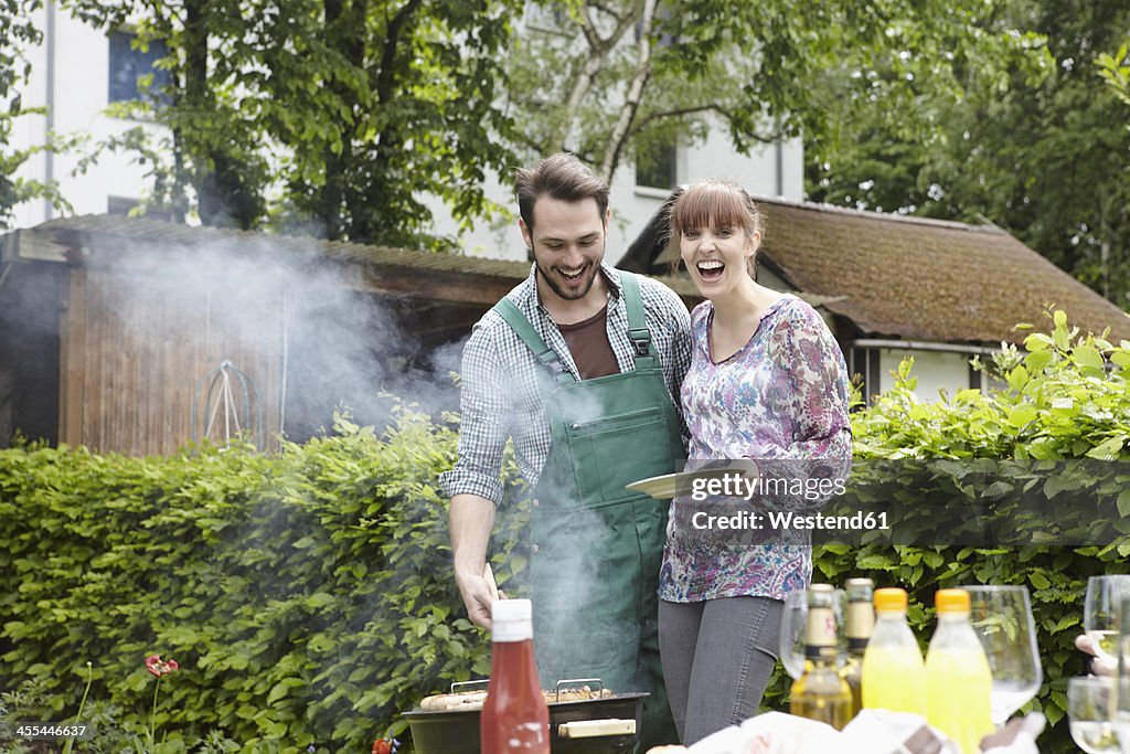 Germany, Cologne, Young couple barbecueing, smiling