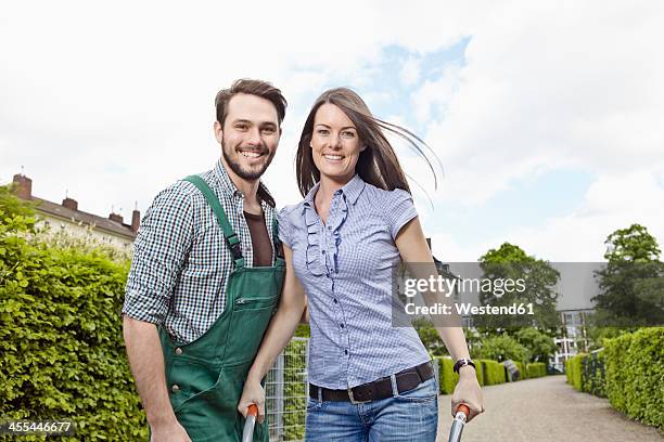 germany, cologne, portrait of young couple with wheelbarrow, smiling - jeans latzhose frau stock-fotos und bilder
