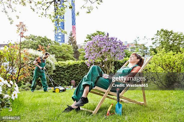 germany, cologne, young woman relaxing on deck chair while man mowing lawn - lawnmowing stock pictures, royalty-free photos & images