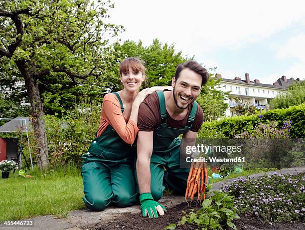germany, cologne, portrait of young couple holding bunch of carrots, smiling - couple gardening stock pictures, royalty-free photos & images