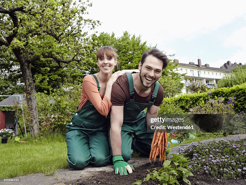 Germany, Cologne, Portrait of young couple holding bunch of carrots, smiling