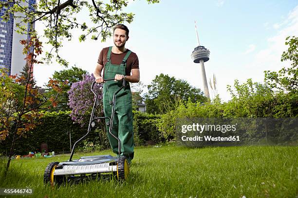 germany, cologne, young man mowing lawn with push mower - dungarees stock-fotos und bilder