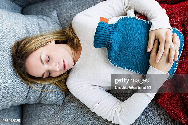 germany, bavaria, munich, young woman sleeping on couch with hot water bottle - clasped hands stock-fotos und bilder