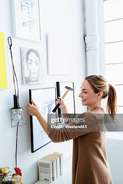germany, bavaria, munich, young woman holding picture frame in front of wall - hanging stock-fotos und bilder