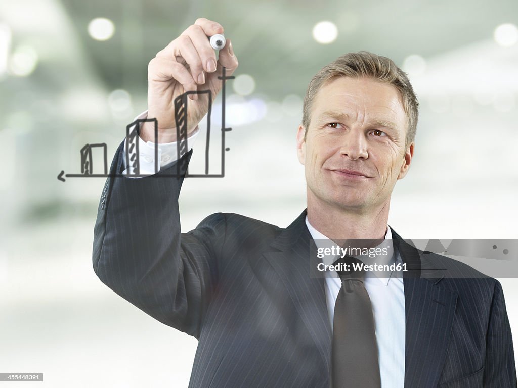 Businessman drawing bar chart on glass, smiling