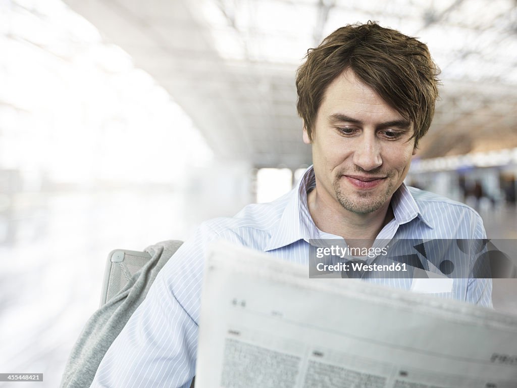 Businessman readig newspaper at airport, smiling