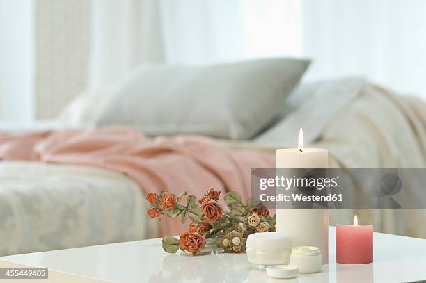 candles, skin cream and bunch of roses on table with bed in background - flower bed stockfoto's en -beelden