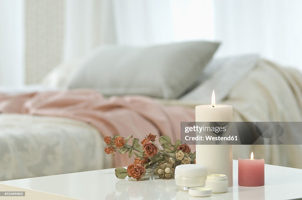 Candles, skin cream and bunch of roses on table with bed in background