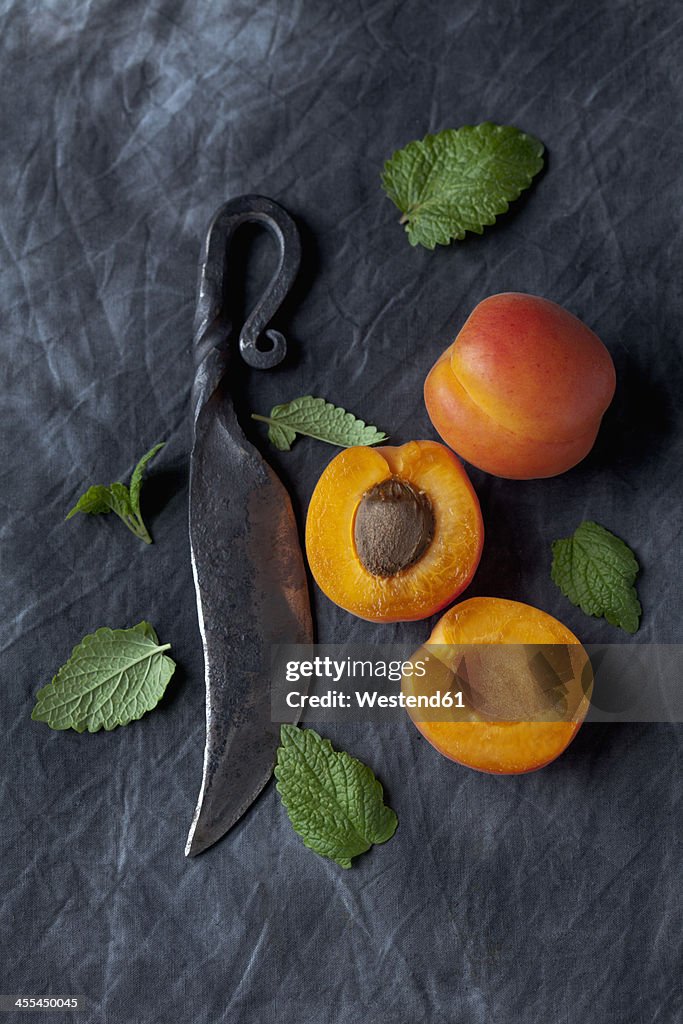 Apricots with leaves and knife on black textile, close up